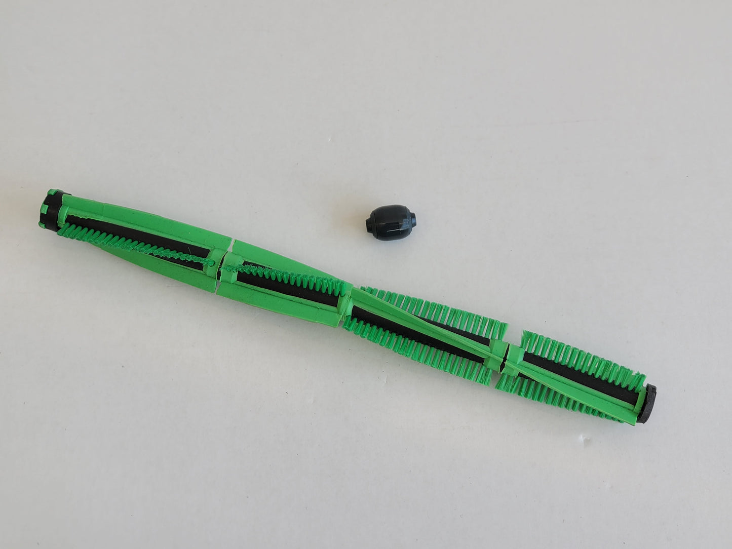 Eine grüne zylindrische RMO Bürstenwalze Frontrolle, kompatibel mit der Vorwerk Elektrobürste EB 400, mit schwarzen Borsten und Kappe, liegt freistehend auf einer weißen Fläche, wobei sowohl die segmentierte Bürste als auch die Kappe deutlich sichtbar sin
