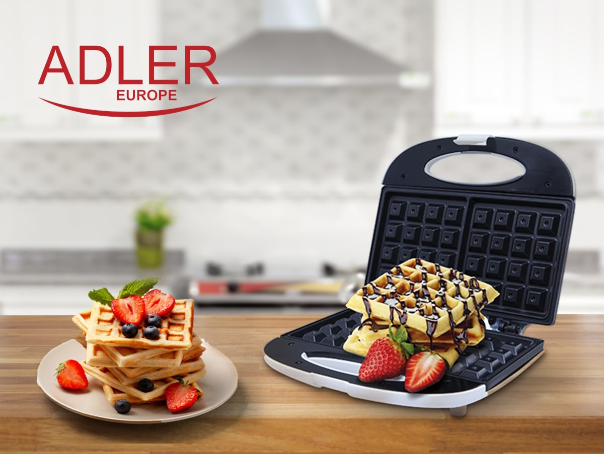 Eine Küchenarbeitsplattenszene mit einem offenen Adler Waffeleisen von immer-saugut, mit Antihaft-Beschichtung und Cool-Touch-Kunststoffgehäuse, präsentiert frisch gebackene knusprige Waffeln mit Schokoladensoße und Erdbeeren. Daneben liegt ein Teller mit