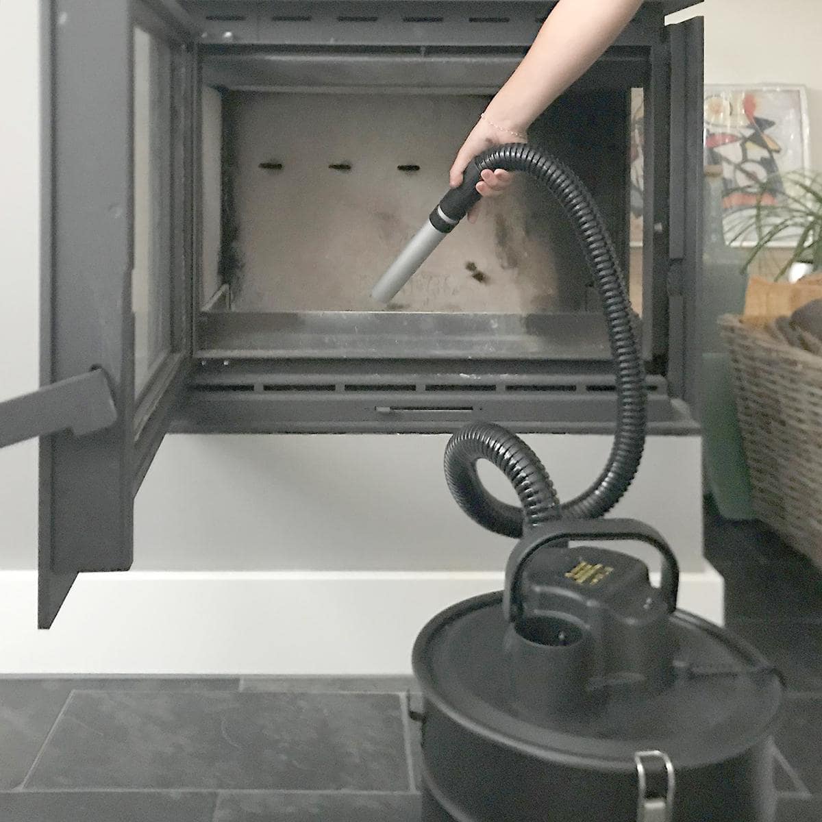Eine Person verwendet einen Schlauch, der an einen Tauchsauger Nedis – Aschesauger ohne Beutel – 800 W, 18 l Staubkapazität, Hepa-Filter, Schwarz angeschlossen ist, um das Innere eines Kamins zu reinigen. Der Vakuumschlauch wird in den Kamin eingeführt, w