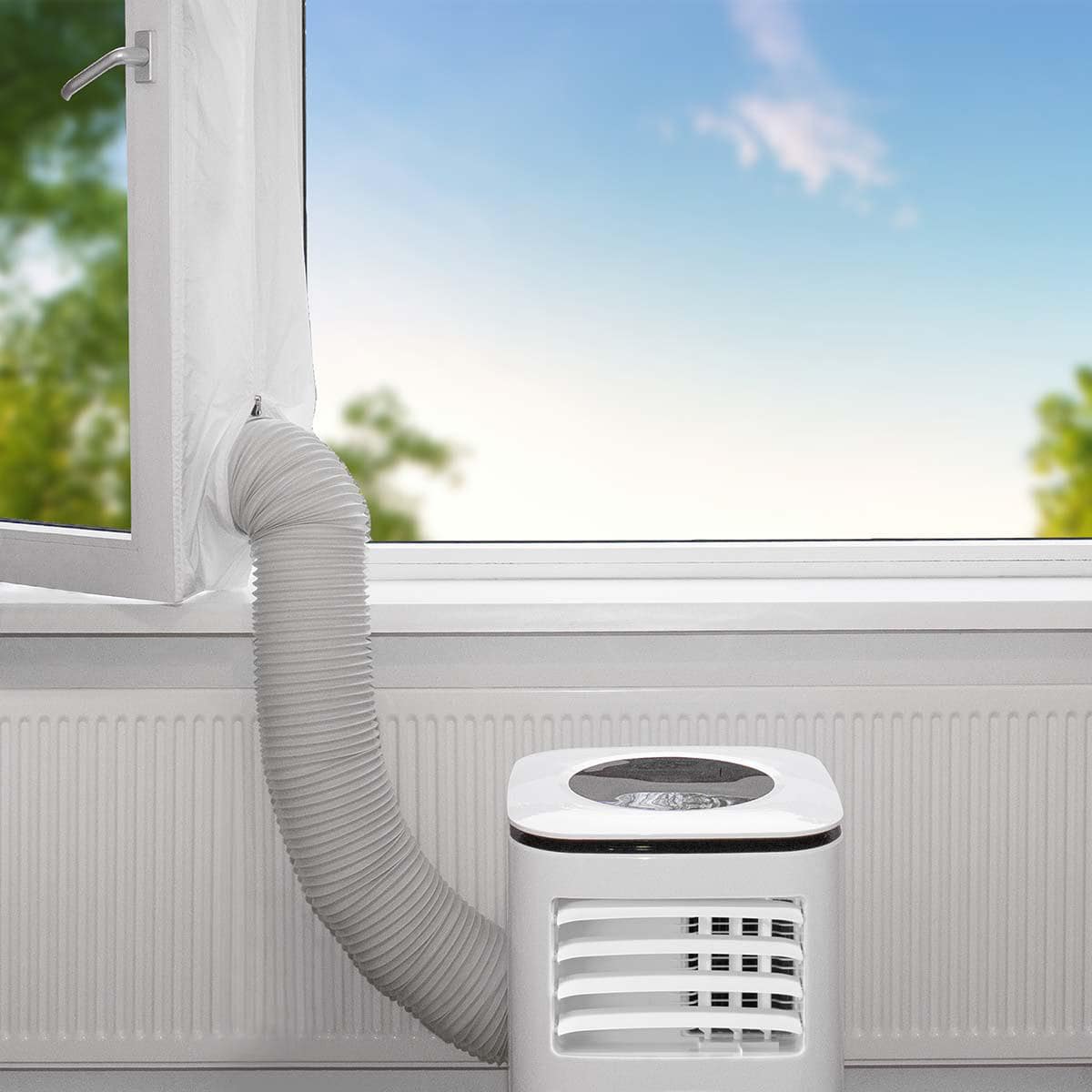 Eine mobile Klimaanlage wird an einer Fensterbank aufgestellt, wobei ein flexibler Abluftschlauch durch das Immersaugut Nedis – Fensterdichtung für Klimaanlagen – Abluftschlauch, Länge 400 cm, einfache Installation zum offenen Fenster führt. Die Außenansi