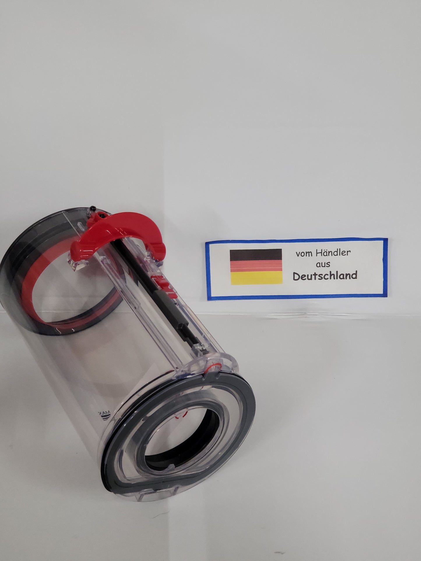 Ein klarer zylindrischer Behälter von ALMEc Supplies, kompatibel mit Dyson V15 Detect Total Clean und V15 Detect Fluffy, mit roten und schwarzen Teilen, liegt vor weißem Hintergrund. Daneben ein Schild "vom Händler aus Deutschland" mit deutscher Flagge.