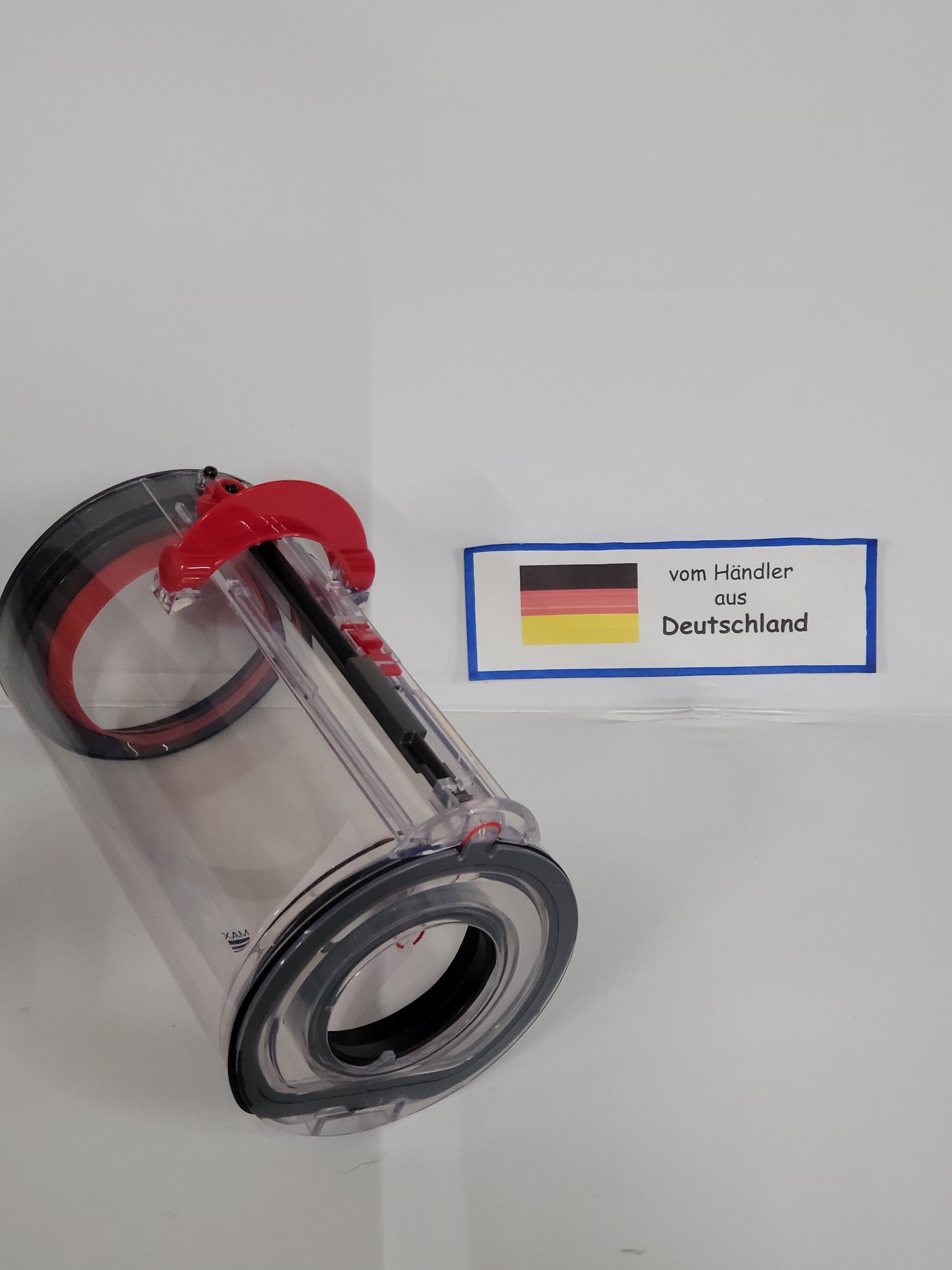 Ein klarer zylindrischer Behälter von ALMEc Supplies, kompatibel mit Dyson V15 Detect Total Clean und V15 Detect Fluffy, mit roten und schwarzen Teilen, liegt vor weißem Hintergrund. Daneben ein Schild "vom Händler aus Deutschland" mit deutscher Flagge.