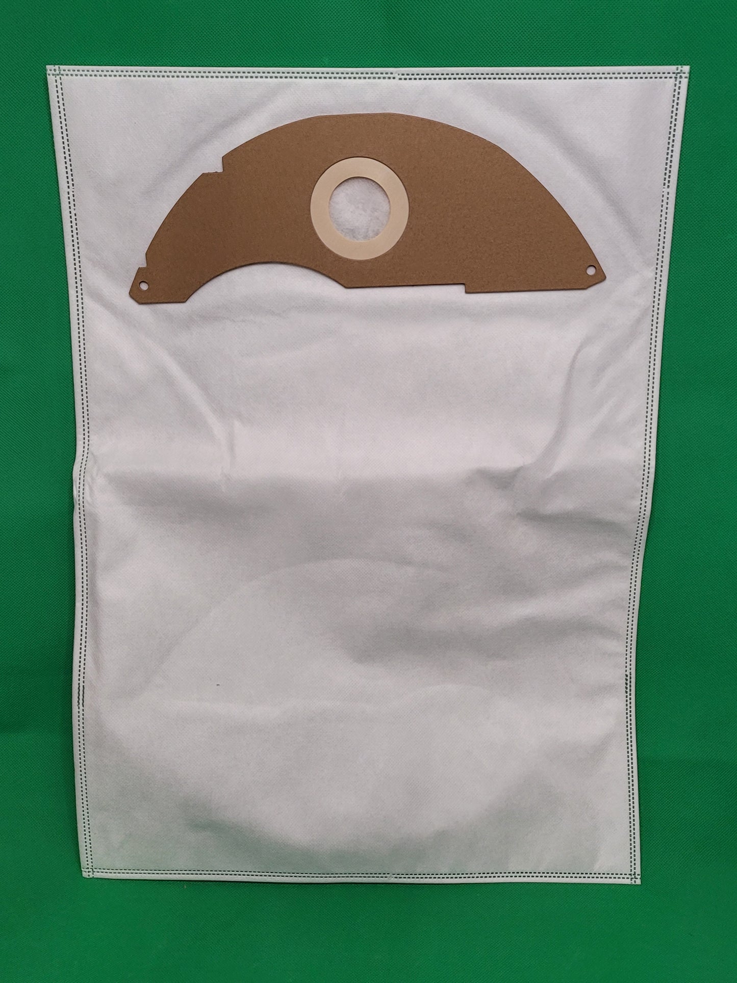 Ein großer weißer Staubsaugerbeutel von immer-saugut mit genähten Rändern liegt flach auf grünem Grund. Am oberen Rand sitzt ein brauner Kartonring passend für Kärcher ProNT 600, 10 Beutel, kompatibel mit 2.889-217.0.