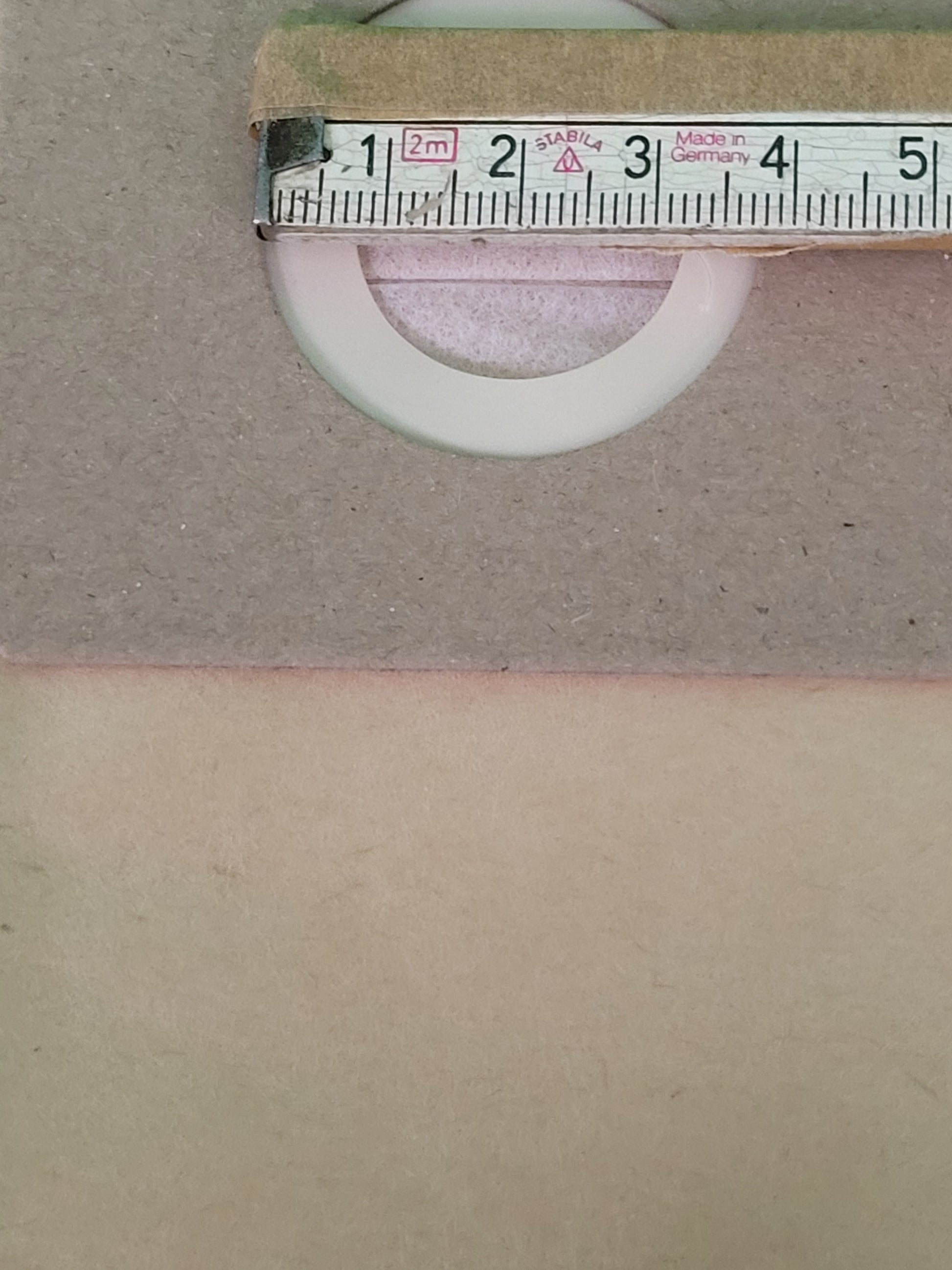 Ein metallenes Maßband markiert 4 cm am oberen Rand des Bildes und ruht auf einer rosafarbenen Oberfläche. Darunter befindet sich ein Ring aus einem immer-saugut 20 Beutel kompatibel mit Güde GNTS 12L Staubsaugerbeutel, der teilweise durch ein Loch im Kar