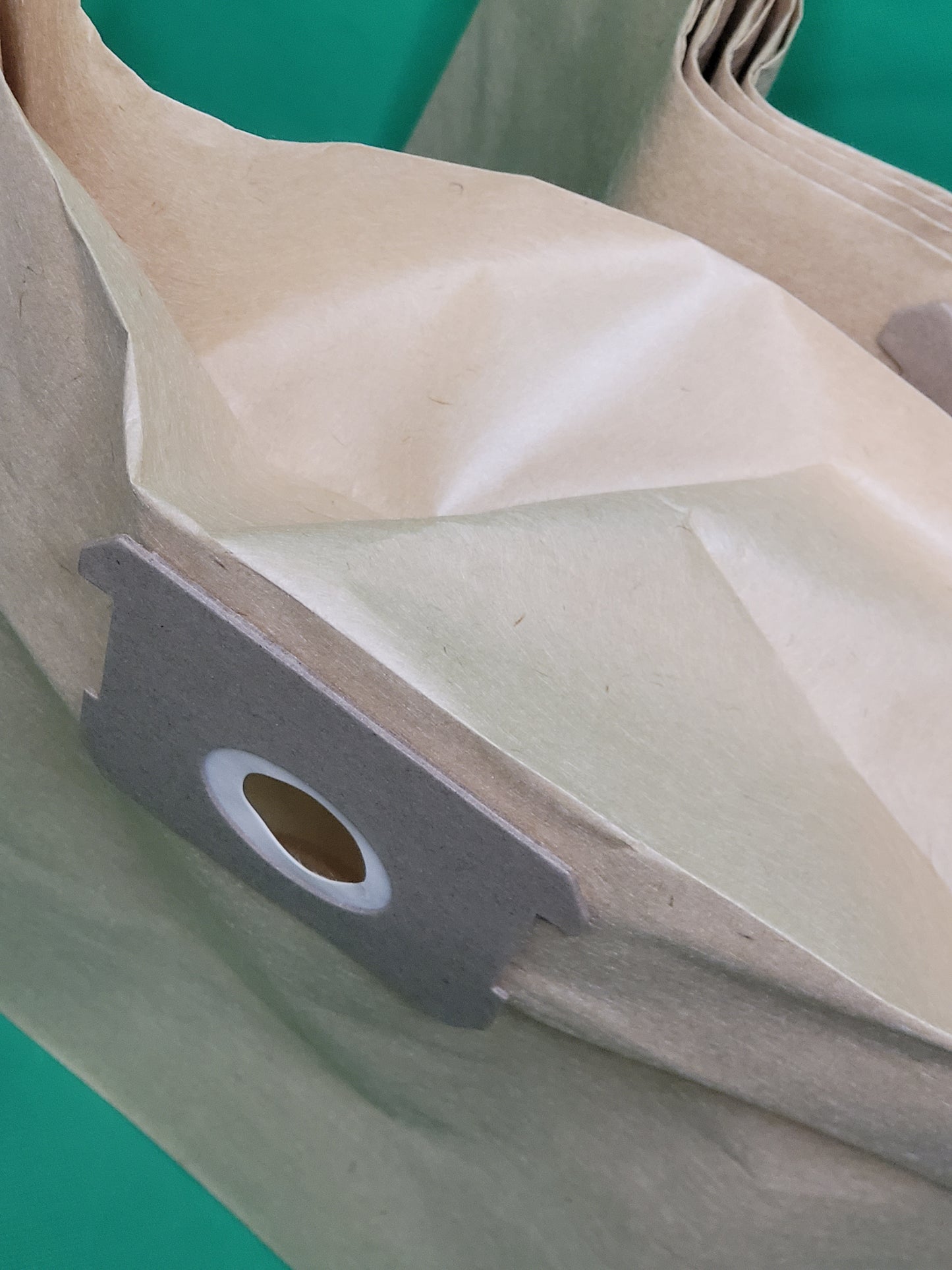 Nahaufnahme von mehreren gefalteten braunen Papiervakuumbeuteln mit Pappkragen und weißem Kunststoffring. Diese 10 Beutel von immer-saugut sind kompatibel mit Parkside PNTSA 20 L, PNTSA 20 Li A1. Solider grüner Hintergrund.