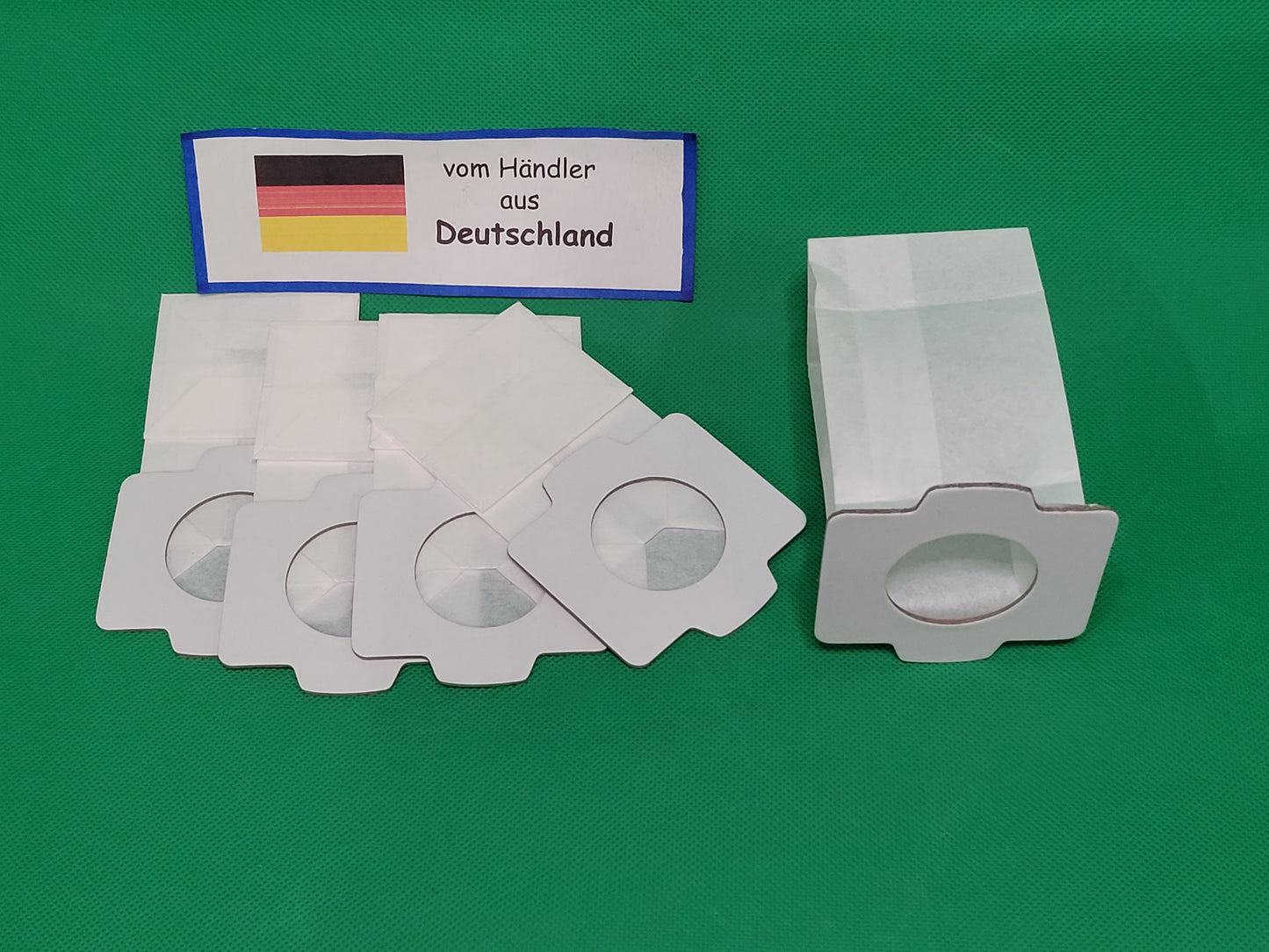 Zehn weiße rechteckige Staubsaugerbeutel von immer-saugut, kompatibel mit Makita 194566-1/198745-3, sind mit runden Pappeinlässen auf einer grünen Fläche abgebildet. Darüber befindet sich ein Etikett mit der deutschen Flagge und der Aufschrift "vom Händle