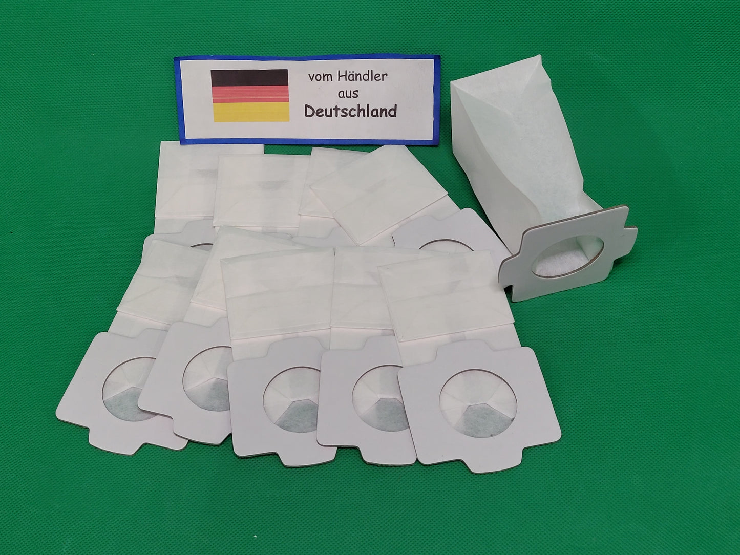Fünfzig weiße immer-saugut Staubsaugerbeutel kompatibel mit Makita 194566-1, 198745-3 mit runden Öffnungen sind auf einer grünen Fläche platziert. Ein Schild mit der deutschen Flagge und "vom Händler aus Deutschland" weist auf den deutschen Standort des V