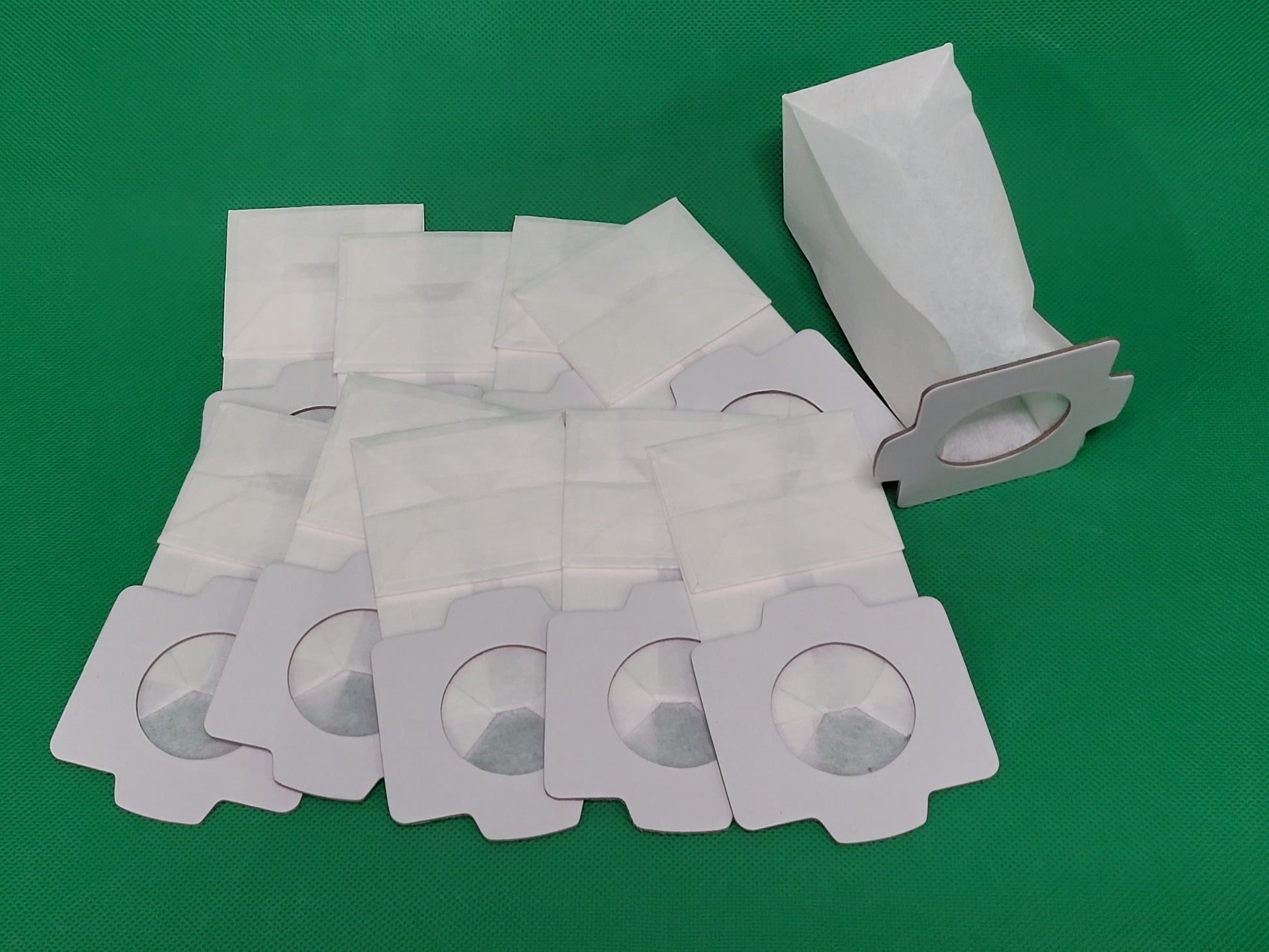 Zehn weiße Staubsaugerbeutel, kompatibel mit Makita 4013D, 4072D, 4076DW, 4076DWR, 4076D, 4030D und 4073D (Marke: Unbekannt/Sonstige), sind auf einer grünen Fläche gestapelt; eine ist geöffnet und zeigt das Innenfach.