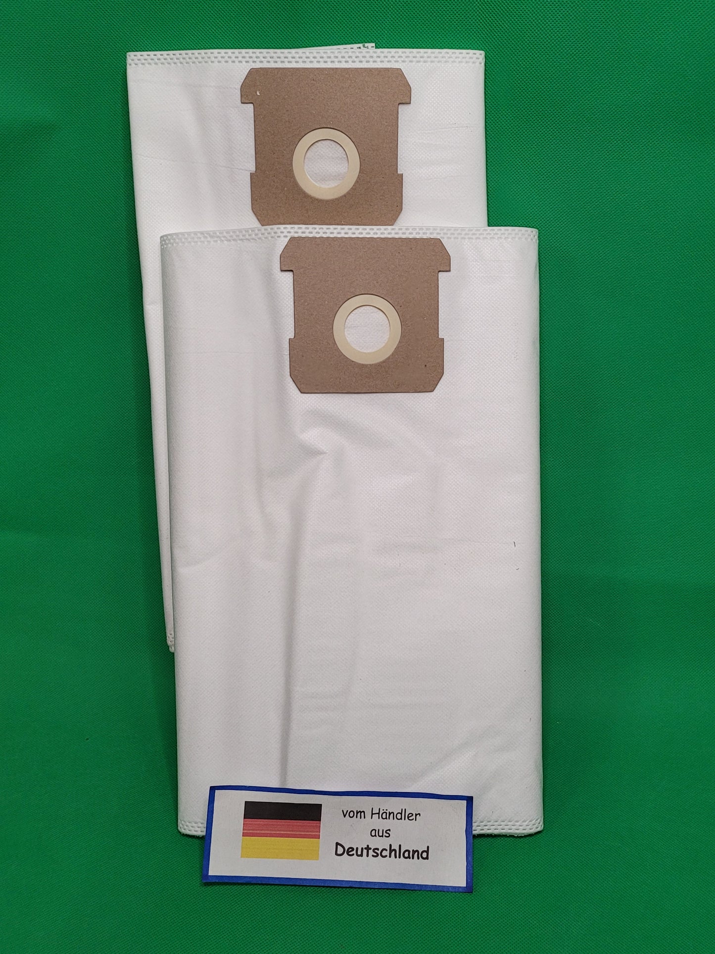 Vor grünem Hintergrund liegen 20 weiße Vlies-Staubsaugerbeutel von Unbekannt/Sonstige, kompatibel mit Einhell TC-VC 1812S, TC-VC 1815S und TE-VC 18/10 Li Solo Power X Change. Ein Kärtchen "vom Händler aus Deutschland" ist davor platziert.