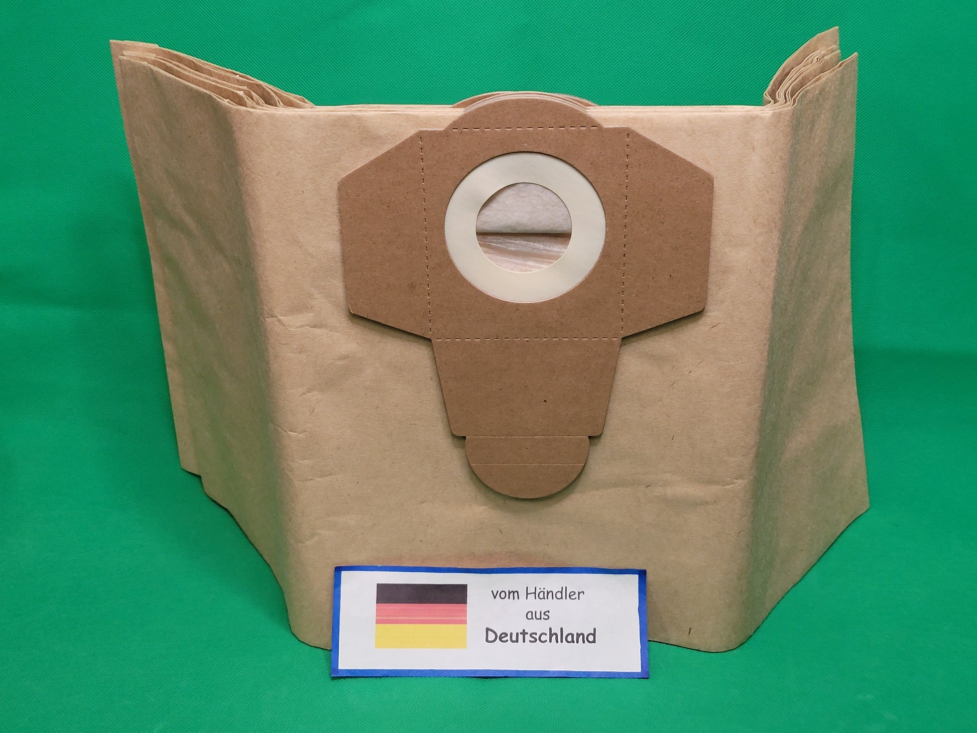 Ein brauner Papier Staubsaugerbeutel von immer-saugut, passend für 20 Liter Einhell Sauger, steht vor grünem Hintergrund. Davor ein Schild mit deutscher Flagge und "vom Händler aus Deutschland" Text. Packung: 20 Beutel.