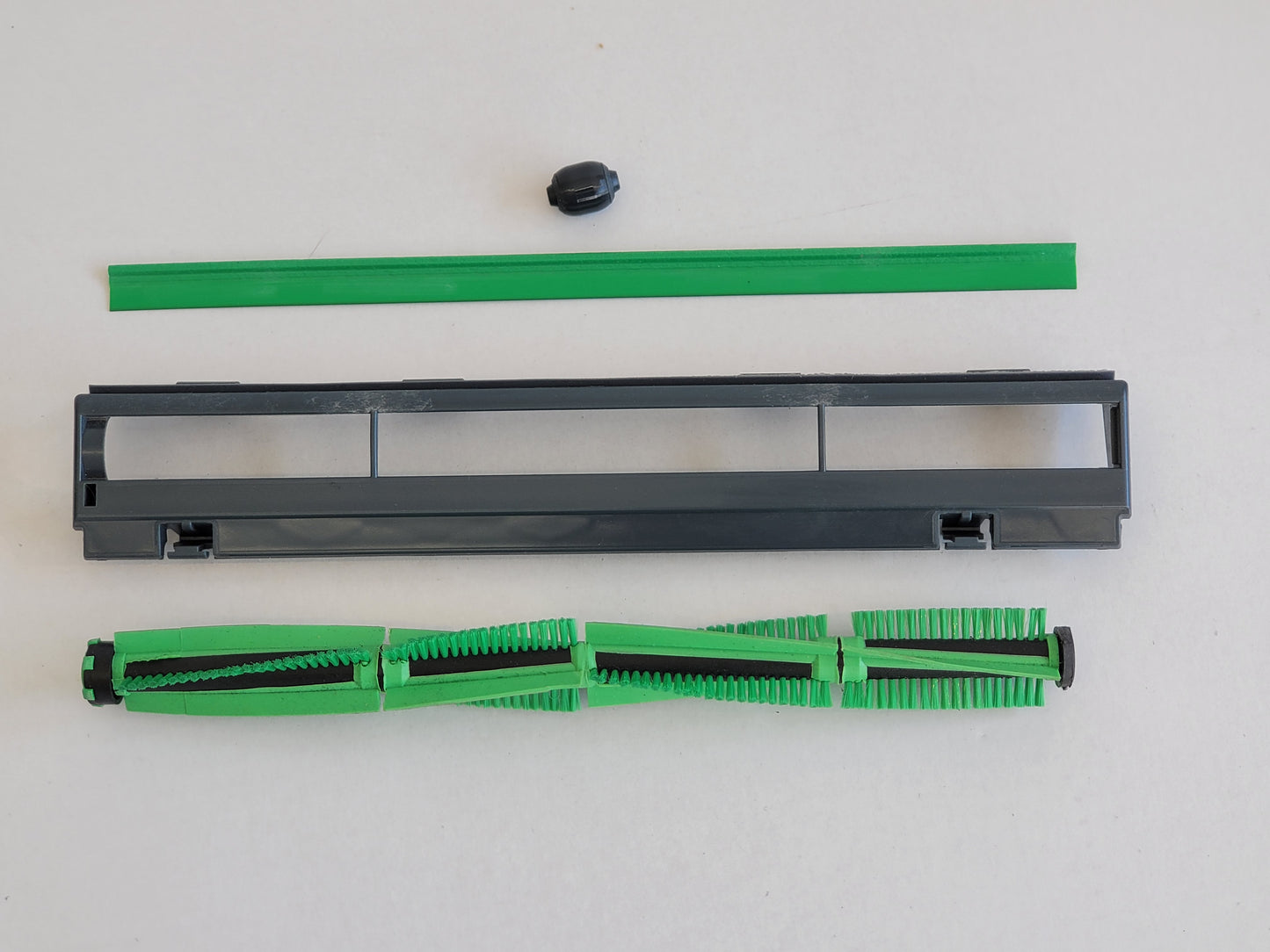 Eine demontierte Bürstenwalze Dichtlippe Rad Abdeckung, kompatibel mit Vorwerk Elektrobürste EB 400 von RMO, wird auf einer weißen Fläche zusammen mit einer grünen Dichtung, einer kleinen schwarzen Kappe, einer grauen Rahmenabdeckung und einer Walze mit a