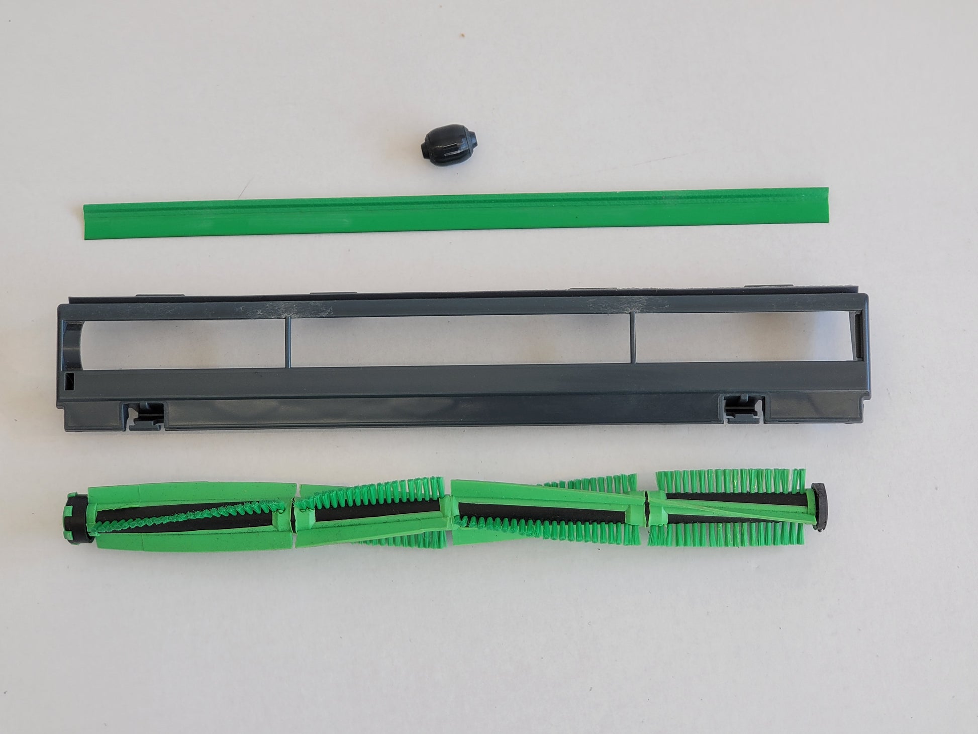 Eine demontierte Bürstenwalze Dichtlippe Rad Abdeckung, kompatibel mit Vorwerk Elektrobürste EB 400 von RMO, wird auf einer weißen Fläche zusammen mit einer grünen Dichtung, einer kleinen schwarzen Kappe, einer grauen Rahmenabdeckung und einer Walze mit a