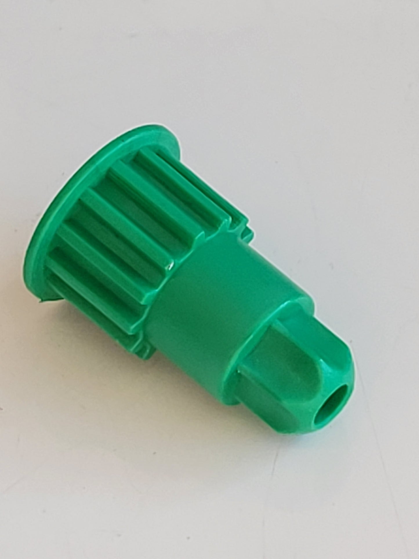 Eine grüne RMO-Antriebsritzel aus Kunststoff, kompatibel mit Vorwerk EB 400, mit gerippter zylindrischer Oberseite, flachem Rand und sechseckigem Ende mit Loch. Dieses Ersatzteil ist auf einer weißen Fläche liegend abgebildet.