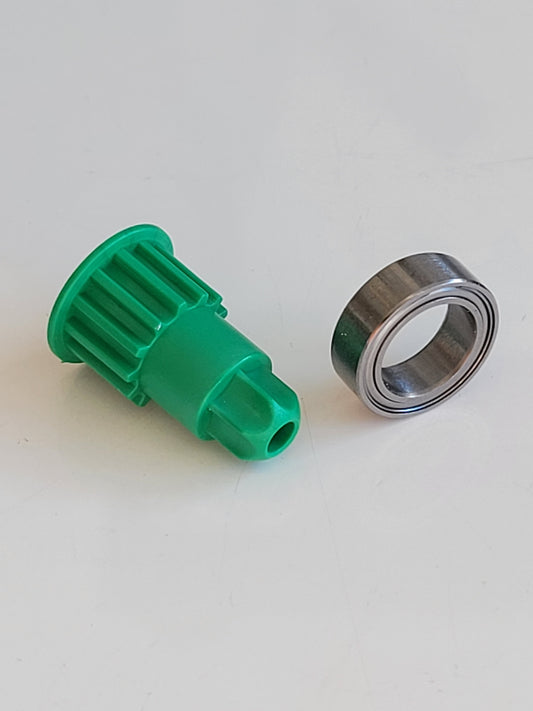 Eine grüne RMO-Antriebsritzel aus Kunststoff (Ritzel Innen- und Außenlager mit Vorwerk EB 400 kompatibel) mit gebördelten, gekappten Enden sitzt neben einem silbernen Metalllager auf einer weißen Fläche.