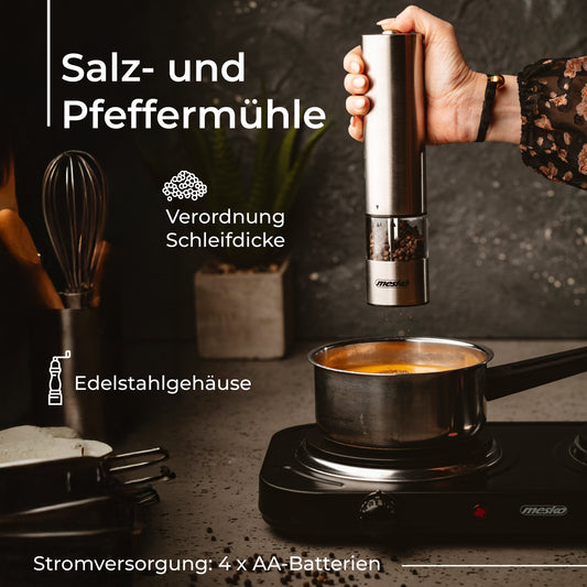 Eine Hand hält eine elektrische Pfeffermühle bzw. Salzmühle der Firma Adler Europe GmbH – deren Edelstahlgehäuse zu sehen ist –, während sie über einem Topf auf einem tragbaren Kocher verwendet wird. Der deutsche Text beschreibt Merkmale wie die Mahlgradeinstellung, das Edelstahlgehäuse und den Betrieb mit 4 AA-Batterien. Im Hintergrund sind eine Holzarbeitsplatte und ein Handtuch zu sehen.