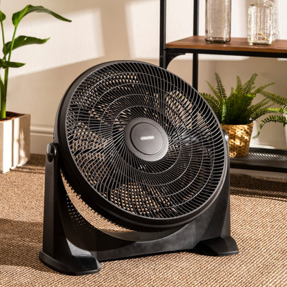 Ein großer schwarzer **immer-saugut Mesko - Bodenventilator - 3 Leistungsstufen, XXL Rotor 50 cm, Neigungsfunktion** mit einstellbarem Neigungskopf steht auf einem beigen Teppich in einem gut beleuchteten Raum. Hinter dem Ventilator steht links eine Topfp