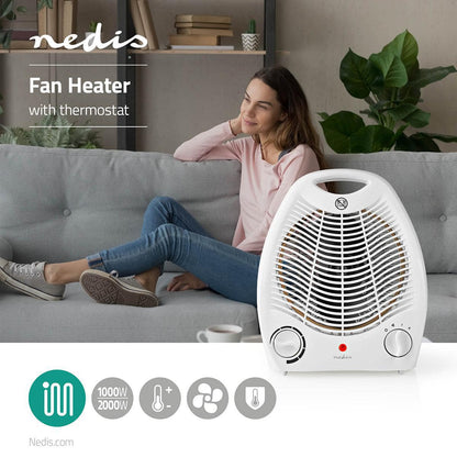 Eine Frau in einem rosa Pullover und blauen Jeans sitzt gemütlich auf einem hellgrauen Sofa. Im Vordergrund steht ein weißer Heizlüfter von Nedis GmbH mit Thermostat auf einem Tisch. Der Heizlüfter verfügt über einen Leistungsregler mit 1000 W- und 2000 W