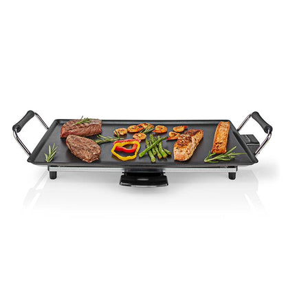 Ein rechteckiger Nedis Teppanyaki-Tischgrill von immer-saugut mit coolen schwarzen Griffen präsentiert eine Reihe von Grillgerichten. Es gibt drei Fleischstücke, zwei Lachsscheiben, mehrere Garnelen, Paprika und Spargelstangen. Die Grillplatte verfügt übe