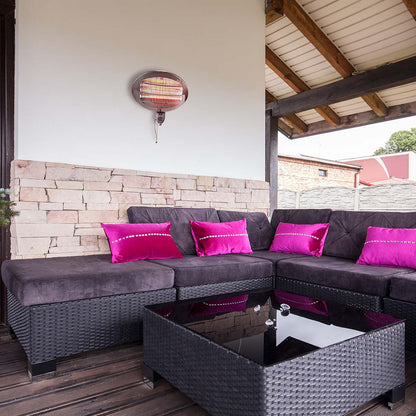 Ein gemütlicher Sitzbereich im Freien verfügt über ein dunkles Korbsofa mit Kissen in leuchtendem Lila und Magenta. Vor dem Sofa steht ein quadratischer Korb-Couchtisch mit Glasplatte. Der Raum ist teilweise umschlossen, mit einer Akzentwand aus Stein und