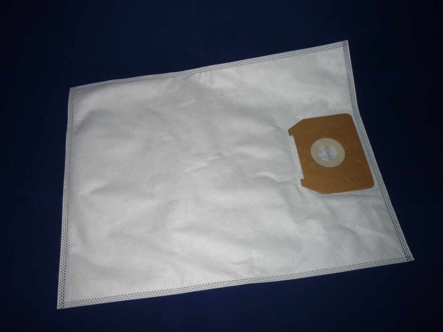 Ein weißer, rechteckiger Staubbeutel von Unbekannt/Sonstige, passend zum Scheppach Nass- und Trockensauger 'PN-NTS20' 1200 W, liegt flach auf, hat einen genähten Rand und einen braunen Pappstecker mit der Modellbezeichnung.
